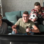 Trois amis regardant un match de football via IPTV dans salon moderne avec bières et ballon