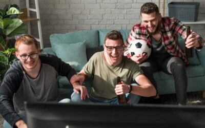 Trois amis regardant un match de football via IPTV dans salon moderne avec bières et ballon