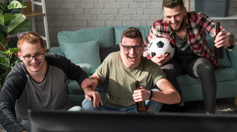Trois amis regardant un match de football via IPTV dans salon moderne avec bières et ballon