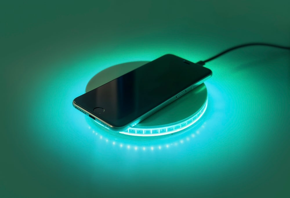 Un "chargeur sans fil" posé sur une table, avec un iPhone qui se recharge, un exemple d'un "chargeur sans fil" discret et élégant.