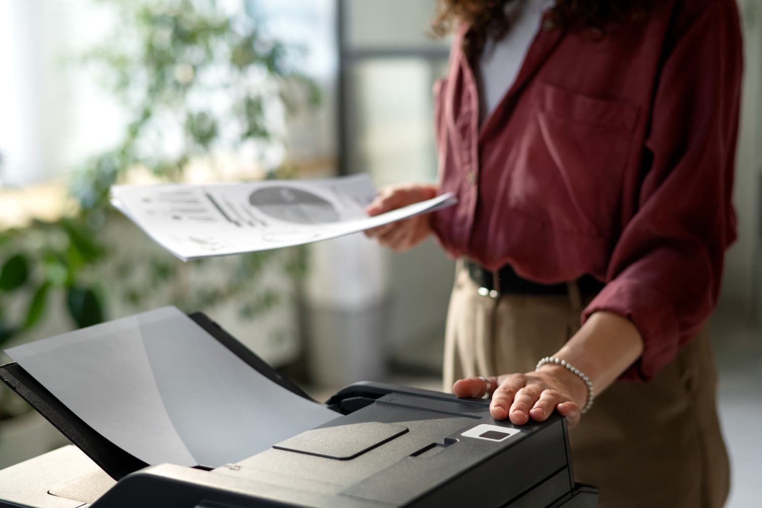 Une personne utilise un photocopieur professionnel pour numériser ou imprimer des documents de bureau, avec un focus sur les mains et les papiers
